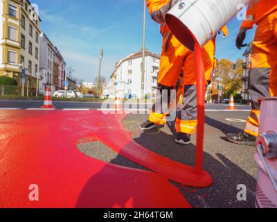 10 novembre 2021, Hessen, Francoforte sul meno: Un lavoratore versa la vernice rossa per il percorso ciclistico sulla superficie di marcatura. Un percorso ciclabile è contrassegnato con vernice rossa in Gartenstraße/Walter-Kolb-Straße. Foto: Andreas Arnold/dpa Foto Stock