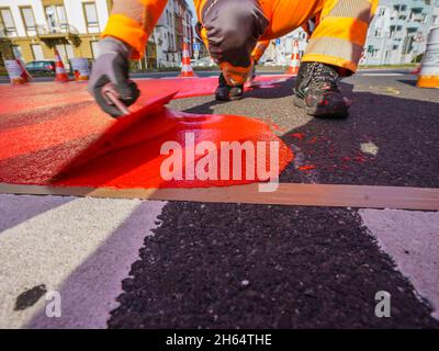 10 novembre 2021, Hessen, Francoforte sul meno: Un operaio dipinge la vernice rossa per la pista ciclabile. In Gartenstraße/Walter-Kolb-Straße un percorso ciclabile è contrassegnato con vernice rossa. Foto: Andreas Arnold/dpa Foto Stock