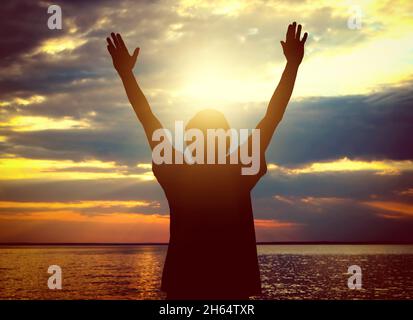 Toned Photo of Happy Man Silhouette con mani in su sullo sfondo del tramonto Foto Stock