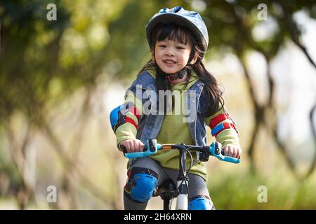 bella ragazza asiatica felice con casco e attrezzatura di protezione completa in bicicletta nel parco della città Foto Stock