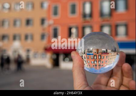 Sfera di vetro di tenuta a mano di fronte a case colorate a Venezia (Italia) Foto Stock