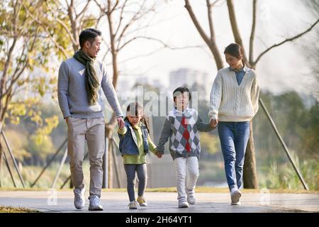 happy famiglia asiatica con due bambini che si prendono una passeggiata all'aperto nel parco della città Foto Stock