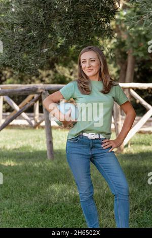 Donne caucasiche di mezza età che indossano t-shirt e jeans rimane con una palla nel parco, tre quarti di colpo Foto Stock