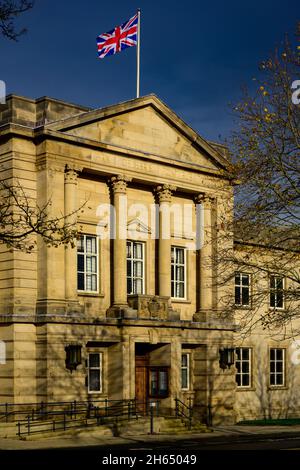 Bandiera Union Jack che sorvola gli uffici del consiglio di Harrogate (flagpole, esterno dell'edificio illuminato dal sole, cielo blu scuro) - Crescent Gardens, Yorkshire Inghilterra, Regno Unito. Foto Stock