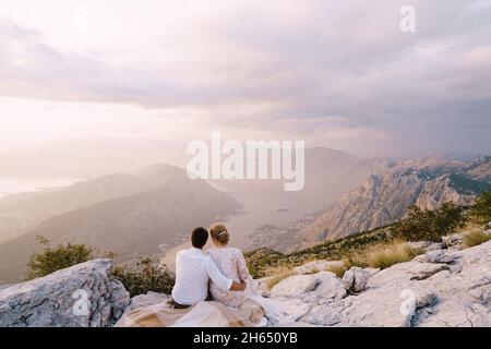 Sposa e sposo siediti sulla montagna e guarda la baia Foto Stock