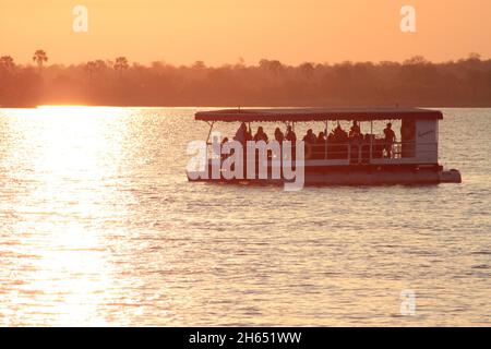 Una grande barca con turisti è visto navigare sul fiume Zambesi al tramonto. Le crociere al tramonto sono popolari sul fiume a Victoria Falls. Zimbabwe. Foto Stock