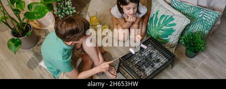 Vista dall'alto dei fratelli che campeggiano a casa tostando marshmallows Foto Stock