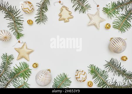 Composizione di Natale o Capodanno. Cornice in rami di abete e decorazioni dorate su sfondo bianco. Disposizione piatta, vista dall'alto, spazio di copia. Foto Stock