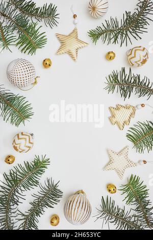 Composizione di Natale o Capodanno. Cornice in rami di abete e decorazioni dorate su sfondo bianco. Disposizione piatta, vista dall'alto, spazio di copia. Foto Stock