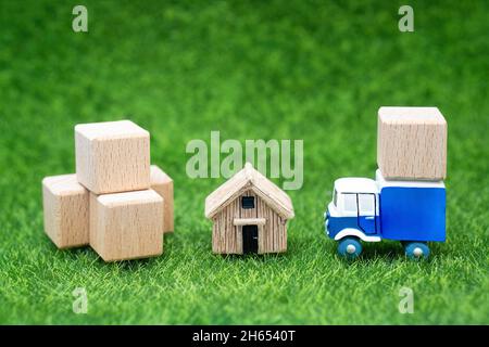 Piccola casa, grandi scatole e un camion giocattolo sul prato. Concetto di servizio di rilocazione della campagna. Foto Stock