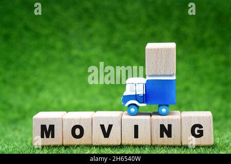 Carrello giocattolo in cima a una fila di blocchi di lettere che legge MUOVENDOSI su uno sfondo verde. Trasferimento in campagna. Foto Stock