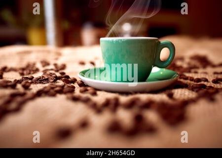 Vista ravvicinata della tazza di caffè calda aromatica e fragrante e dei chicchi di caffè sulla borsa. Caffè, bevande Foto Stock