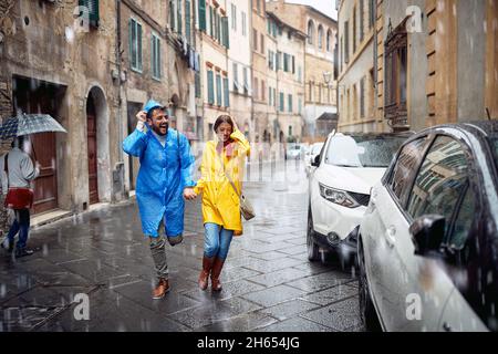 Una giovane coppia di impermeabili in strada sta correndo per nascondersi dalla pioggia in un'atmosfera di fretta. Passeggiata, pioggia, città, rapporto Foto Stock