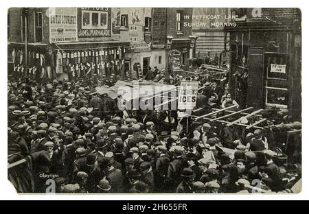 Cartolina originale di auguri dell'epoca edoardiana di tutti gli uomini di folla, classe di lavoro, con cappelli piatti, in Petticoat Lane, abbigliamento in vendita, Domenica mattina, Londra, Regno Unito circa 1907 Foto Stock