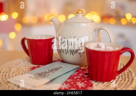 Teiera in ceramica bianca con testo buon Natale e tazze con marshmallows su sfondo bokeh xmas Foto Stock
