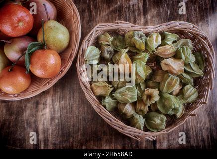 Frutti autunnali in cesto di vimini su un tavolo di legno grunge: Pere e arance mandarini e un mazzetto di physalis alkekengi con il flo secco a campana Foto Stock