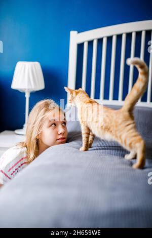 Il gattino dai capelli rossi sul letto si allunga e cammina verso la ragazza. Foto Stock