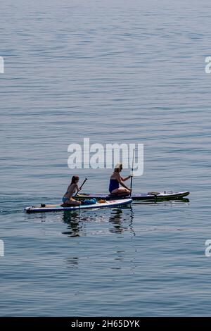 Due femmine di paddleboard in un calmo, caldo giorno di luglio, vicino a Charlestown, Cornovaglia sud, Regno Unito. Foto Stock