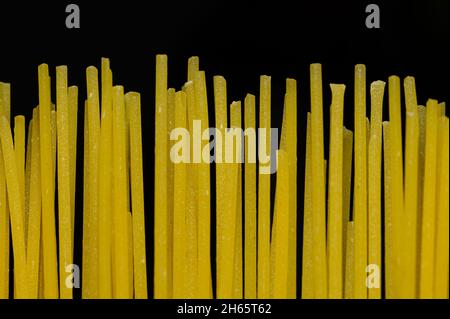 Alcuni spaghetti crudi in posizione verticale di fronte ad uno sfondo nero profondo. Foto Stock