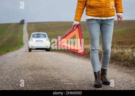 La sicurezza prima di tutto. Macchina rotta sulla strada. Triangolo segnaletico di mantenimento conducente. Sfortuna durante il viaggio. La donna ha bisogno di assistenza stradale dopo un incidente stradale Foto Stock