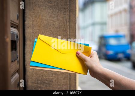 Consegna delle lettere da parte del gestore di posta. Il lavoratore postale inserisce la busta nello slot di caricamento. Donna mano che tiene buste colorate sulla strada della città Foto Stock