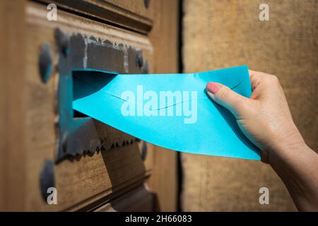 Donna che inserisce la busta blu nello slot di caricamento. Recapito della lettera da parte del corriere. Mano ravvicinata con busta Foto Stock