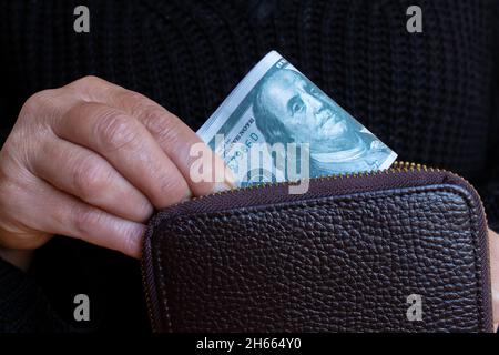 Mano della donna del primo piano che mette le fatture del dollaro nel portafoglio. Può aver ricevuto il suo stipendio o può essere pronta ad andare a fare shopping. Foto Stock