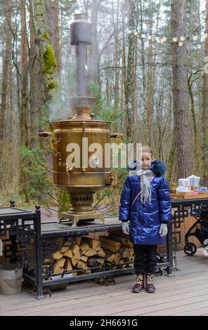 Bambina in piedi vicino enorme tradizionale samovar tè russo in metallo vecchio nella foresta Foto Stock