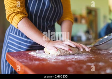 Metà della sezione di donna che indossa l'impasto grembiule su tavola di legno in cucina a casa Foto Stock
