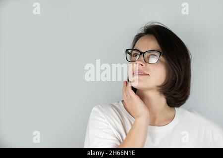 Foto studio su uno sfondo grigio di una bella ragazza sognante sorridente con capelli scuri indossare occhiali Foto Stock