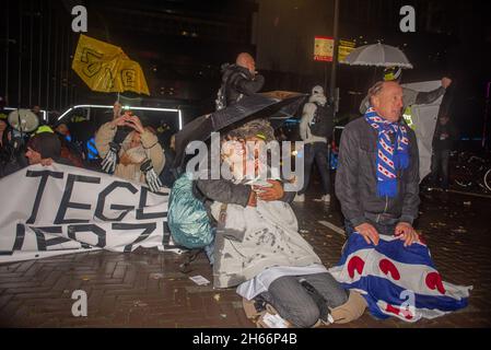 Un manifestante viene coperto dopo essere stato addensato da cannone d'acqua, durante la dimostrazione.gli ufficiali di polizia Riot si trovano di fronte ai manifestanti che si riuniscono all'Aia durante una conferenza stampa del primo ministro olandese Mark Rutte tenuto per annunciare nuove restrizioni del 19. Foto Stock