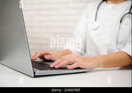 Raccolto della mano di un medico generico, medico, medico che lavora su un computer portatile, scrivere messaggi di testo sulla tastiera, videoconferenza con una te Foto Stock