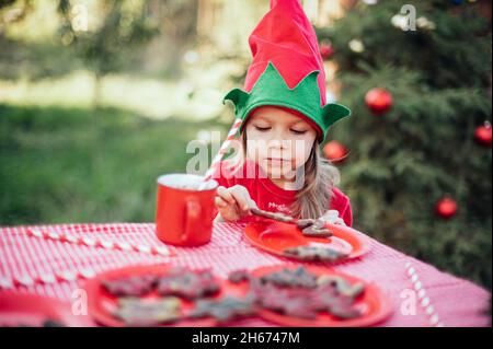 Natale nel mese di luglio. Bambino in attesa di Natale in legno nel mese di luglio. Ritratto di bambina che beve cioccolata calda con marshmallow e zenzero uomo biscotti. Buon Natale e buone feste. Foto Stock