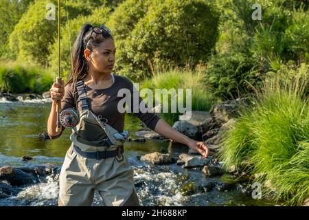 Una giovane donna asiatica in piedi pesca a mosca in un riffle su un fiume Foto Stock