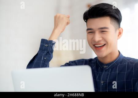 Felice giovane uomo d'affari lavoro su computer portatile finitura con entusiasmo e successo sulla scrivania a casa, uomo d'affari utilizzando notebook con successo e surp Foto Stock