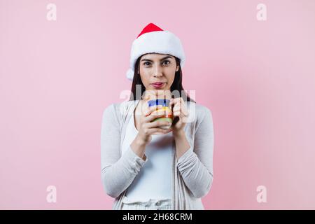 donna di natale ispanica, con una tazza di argilla di caffè o punch di frutta su sfondo rosa in america latina Foto Stock