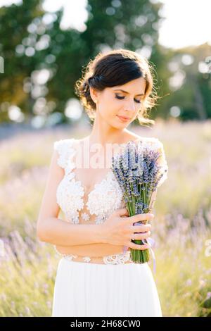 Sibenik, Croazia - 05.06.17: Sposa in un abito in pizzo bianco ha le braccia incrociate sul petto e sta tenendo un bouquet di lavanda in loro, guardando Foto Stock