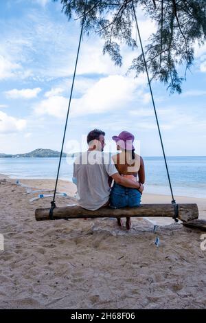 Bang Tao Beach Phuket Thailandia, spiaggia con palme e un uomo e una coppia di donne nell'altalena sulla spiaggia. Concetto di estate, viaggio, vacanza e vacanza - Swing appende da palme da cocco Foto Stock