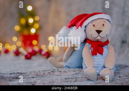 Bambola di orsacchiotto con cappello e scarpetta di santa con bokeh sfondo chiaro dell'albero di Natale. Foto Stock