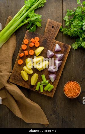 Set vegetariano per zuppa di verdure crude su tagliere di legno. Carote tritate, patate, cipolle rosse, lenticchie, prezzemolo. Preparazione degli ingredienti per Foto Stock