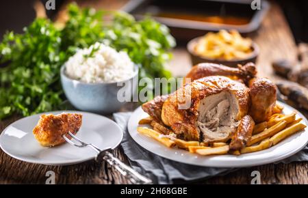Pollo arrosto intero tagliato su una forchetta con contorni, riso e patatine fritte. Foto Stock
