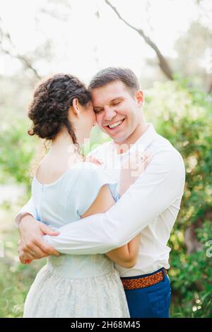 Kotor, Montenegro - 21.06.17: Uomo sorridente abbraccia donna in abito blu mentre si alza in verde uliveto Foto Stock