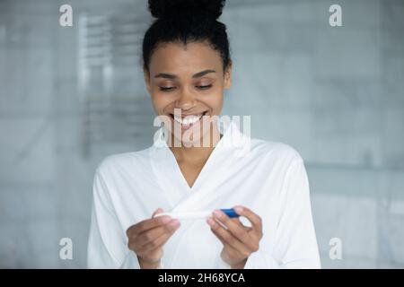 Felice interessato giovane africana mista razza donna utilizzando il test di gravidanza. Foto Stock