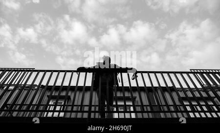 Una foto in scala di grigi di un uomo appoggiato su corrimano in metallo Foto Stock