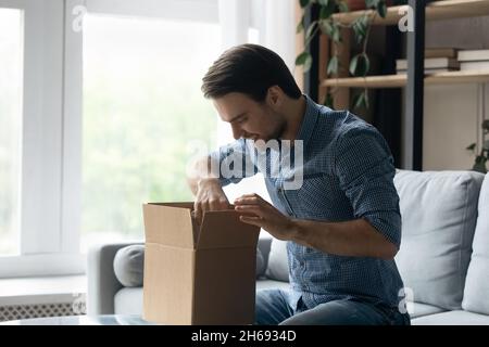 Felice giovane bell'uomo che apre grande scatola di cartone. Foto Stock