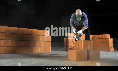 Uomo ha visto blocchi di mattoni. Riprese in stock. Lavoratore professionale per l'approvvigionamento di materiali da costruzione. Costruttore in elmetto utilizzando la sega speciale è impegnato i Foto Stock