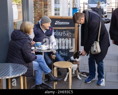 Fotografia di strada Regno Unito; una coppia che ha un caffè con il loro cane da compagnia, e l'uomo che passa da cane da cucciolo - amore britannico dei cani; Cambridge Regno Unito Foto Stock