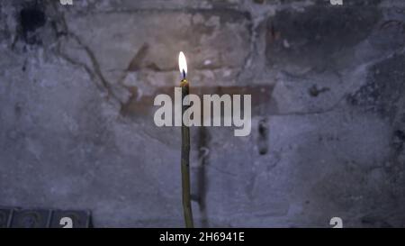 Primo piano di una candela che brucia in una vecchia chiesa. Riprese. Primo piano le bellissime candele bruciate su sfondo grigio scuro parete. Foto Stock