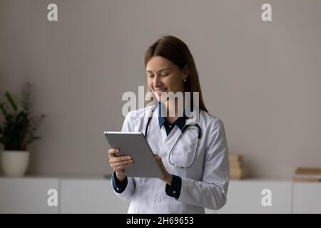 Sorridente medico terapista con tablet, in piedi in ufficio Foto Stock