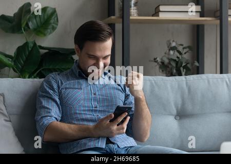 Buon giovane uomo che legge buone notizie sul cellulare. Foto Stock